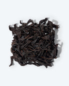 Long, dark Da Hong Pao oolong tea leaves, showing rich brown accents against dark oxidized color on elegantly twisted leaves.